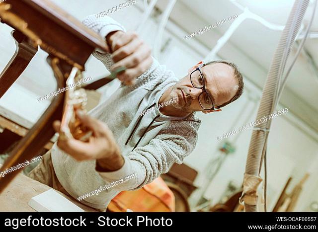 Male expertise applying gold color on antique furniture standing at workshop