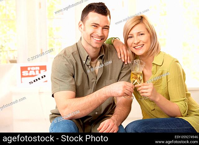 Portrait of happy couple celebrating purchase of new home, laughing at camera