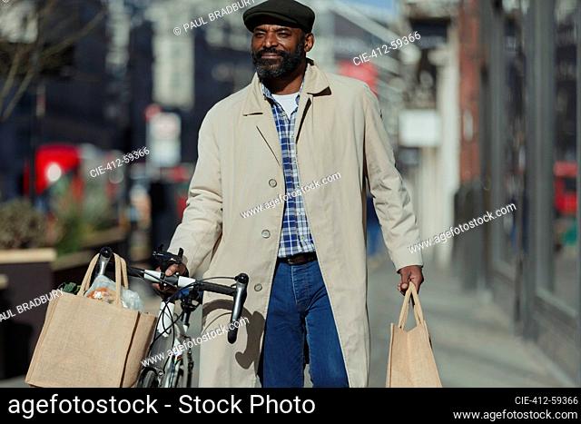 Male tourist with bicycle and grocery bags walking on urban sidewalk