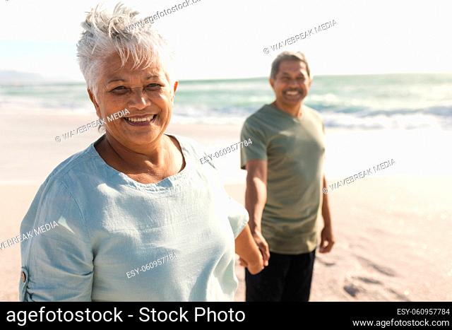 Portrait of smiling senior multiracial woman holding hand with man at beach on sunny day
