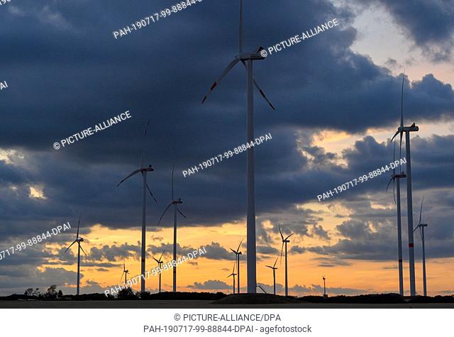 16 July 2019, Brandenburg, Sieversdorf: Shortly after sunset, dark clouds move over the ""Odervorland"" wind energy park in the Oder-Spree district