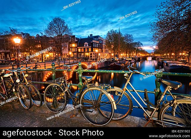 Night view of Amterdam cityscape with canal, bridge with bicycles and medieval houses in the evening twilight illuminated. Amsterdam, Netherlands
