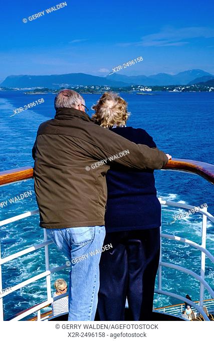 A couple looking back over a ships rail whilst leaving port in the Norwegian fjords