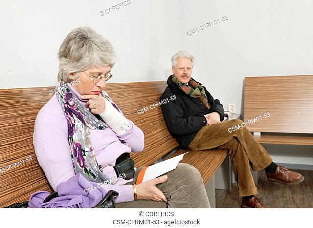 two elderly people sitting in a general practitioner's waiting room, reading various magazines and newspapers