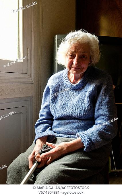 Portrait of old woman at home, sitting by the window, smiling and looking at the camera