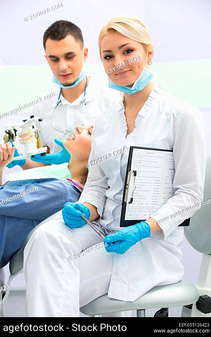 Young dentist working with the patient in a modern hospital. He is assisted by a young girl assistant. The assistant to the card in the hands of the...