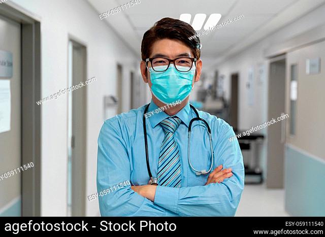Portrait of mixed race male doctor wearing face mask standing in hospital corridor
