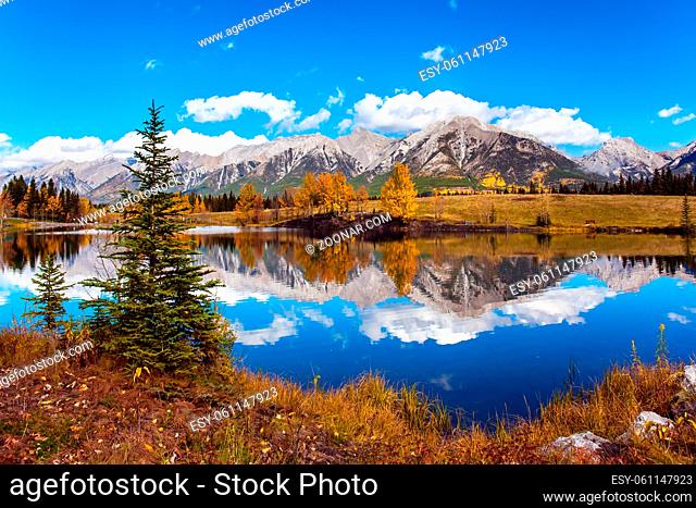 Outskirts of Kenmore. Bright autumn forest is reflected in the lake. Three Sisters Mountain in Canadian Banff Park. The concept of active