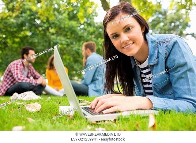 Smiling female using laptop with other students in park