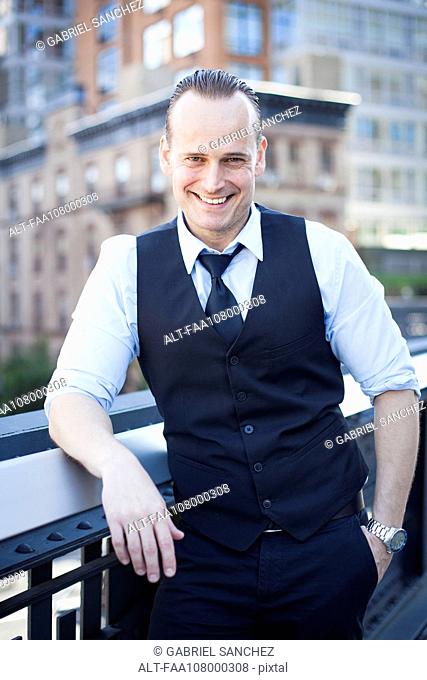 Businessman standing on balcony, smiling, portrait