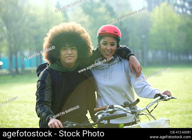 Portrait happy teen couple hugging on bicycles in park