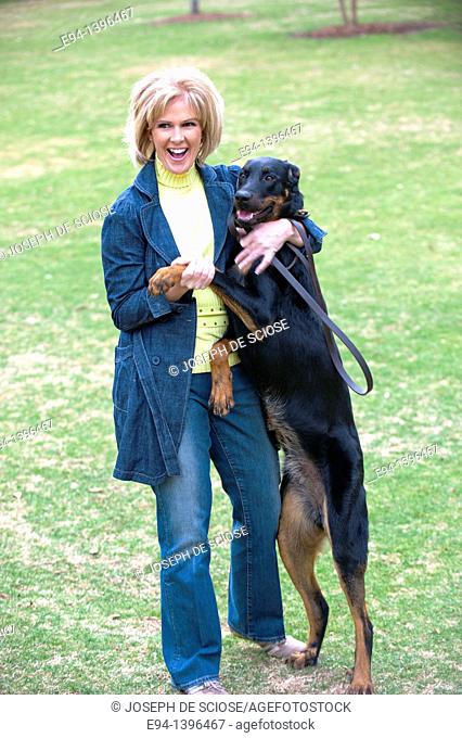 Fifty year old blond woman playing with a Doberman Pinscher in a park