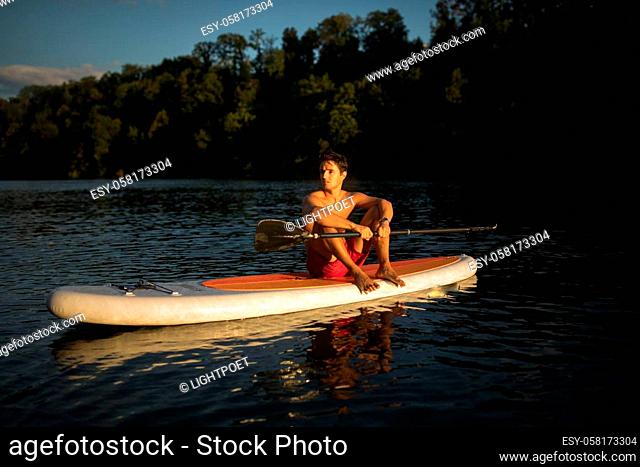 Young man on a paddle board. Getting a great exercise on a lovely river in warm evening sunlight - paddle underwater image