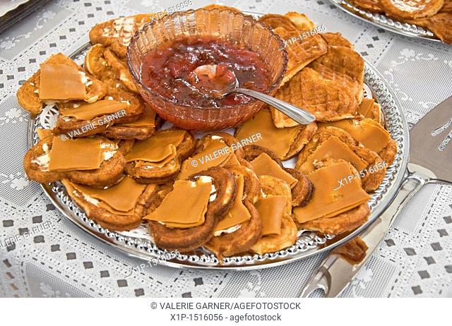 This traditional Norwegian food, is a silver platter of heart shaped waffles with slices of brown goat cheese on top  In the center of the platter is a crystal...