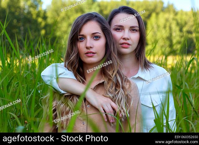 Two young women brunette and blonde are standing in a field. Romantic female couple with closed eyes in tall grass. One girl hugged her girlfriend