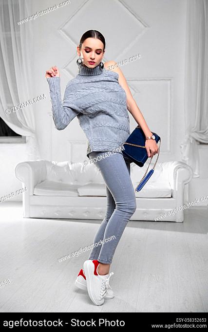 Beautiful woman dressed in a sweater and jeans with a blue clutch in her hands