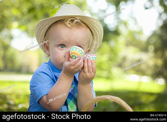 Cute little boy wearing hat enjoying his easter eggs on picnic blanket outside in the park
