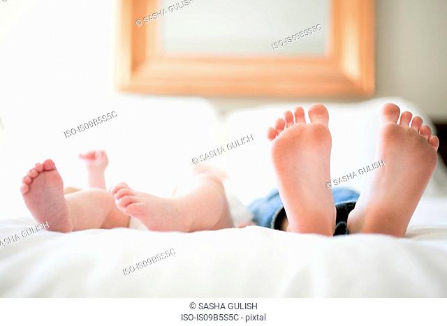 Young girl and baby brother lying on bed, focus on feet