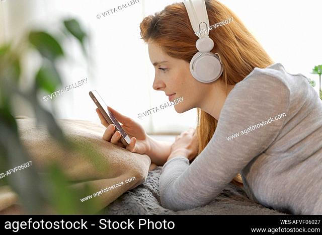 Young woman wearing headphones and using smartphone at home