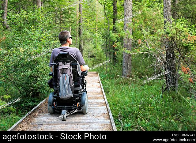Happy man on wheelchair in nature. Exploring forest wilderness on an accessible dirt path
