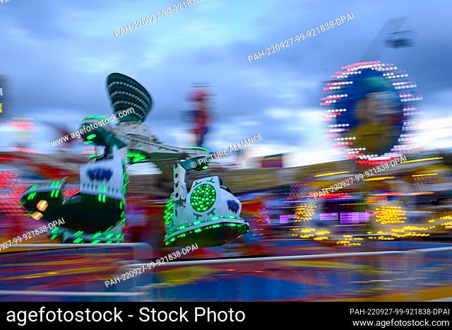 27 September 2022, Saxony-Anhalt, Magdeburg: A carousel turns in the evening at the autumn fair of the capital of Saxony-Anhalt, reflected in a puddle of rain