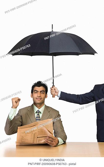 Businessman reading a newspaper under umbrella and clenching fist