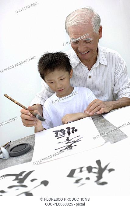 Man and young boy indoors painting Chinese letters