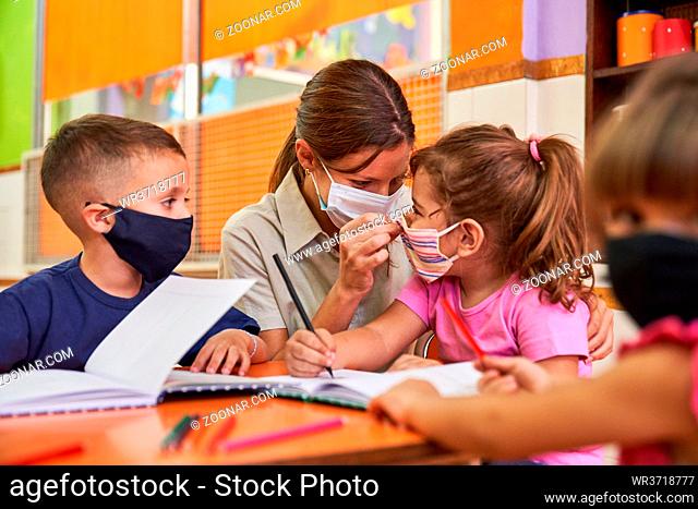 Erzieherin oder Tagesmutter hilft Kindern beim Lernen mit Mundschutz wegen Covid-19