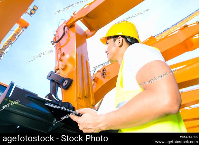Asian worker controlling construction machinery of building site or mining company