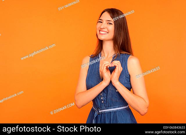 Cheerful pretty woman in dress making heart shape with hands and smiling kindly, showing charity symbol, declaration of love, expressing emotions
