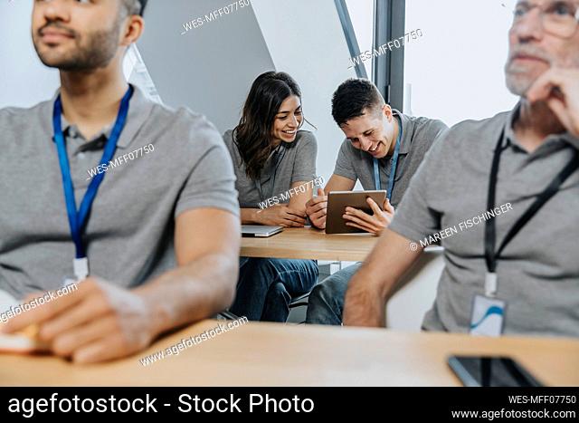 Hombre sonriente con tableta digital por aprendiz en un banco en el aula