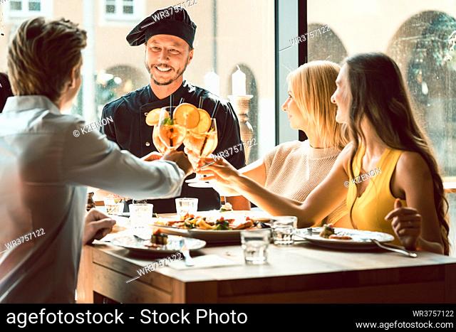 Experienced chef smiling congratulated for the delicious food by four young people at the table of a trendy exclusive restaurant