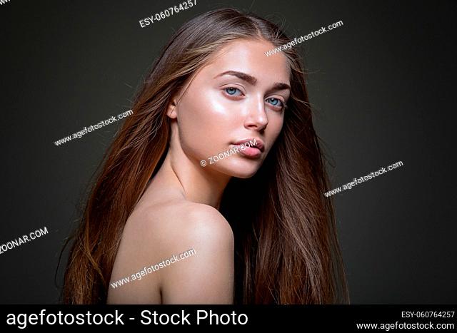 Beautiful young woman with straight healthy hair and natural make-up on dark background. Copy space
