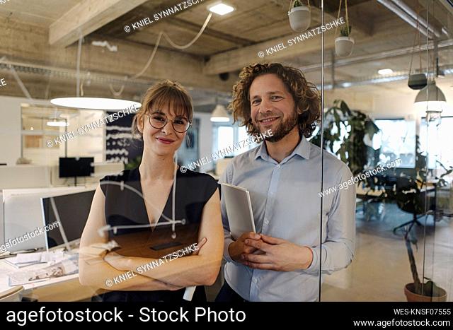 Portrait of confident businessman and businesswoman behind glass pane in office
