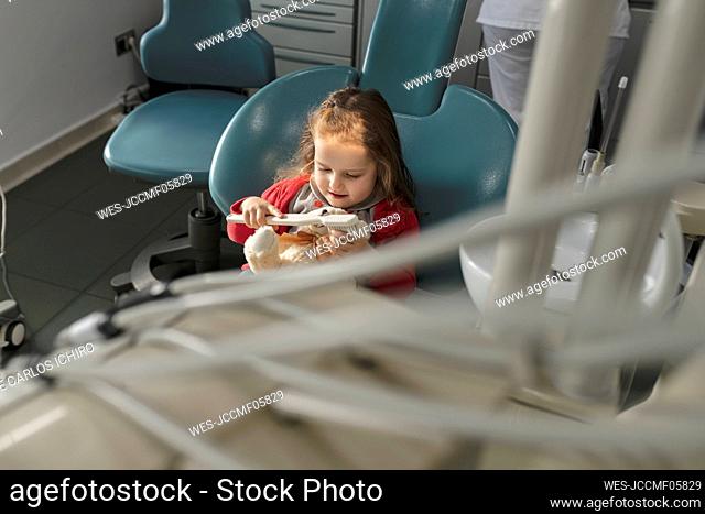 Cute little girl playing with toothbrush at dental clinic