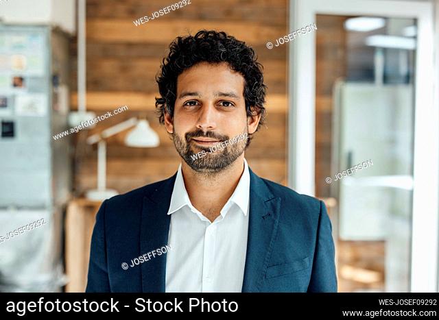 Smiling businessman standing in front of wall in office