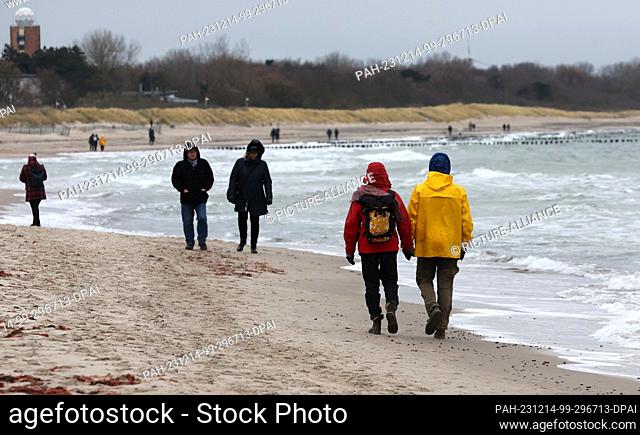 14 December 2023, Mecklenburg-Western Pomerania, Warnemünde: Walkers are out and about on the Baltic Sea beach in gray rainy weather