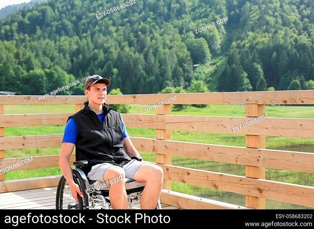 Disabled young man on a wheelchair on a wooden bridge path enjoying in nature