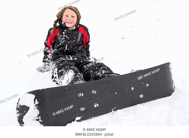 Smiling girl sitting in snow with snowboard