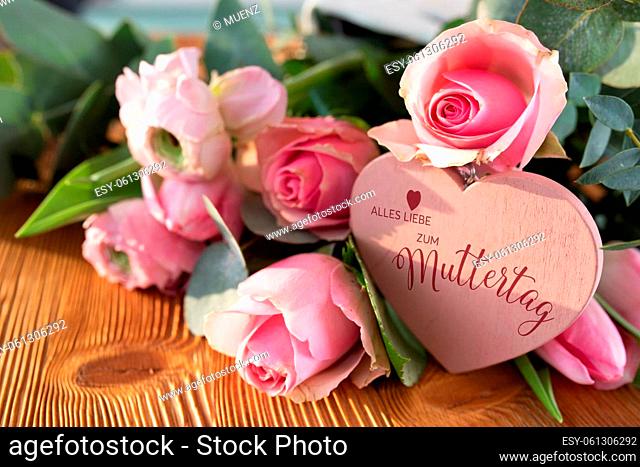 Mothers day card with pink spring flowers and heart shape on rustic wood. Close-up with short depth of field and german text