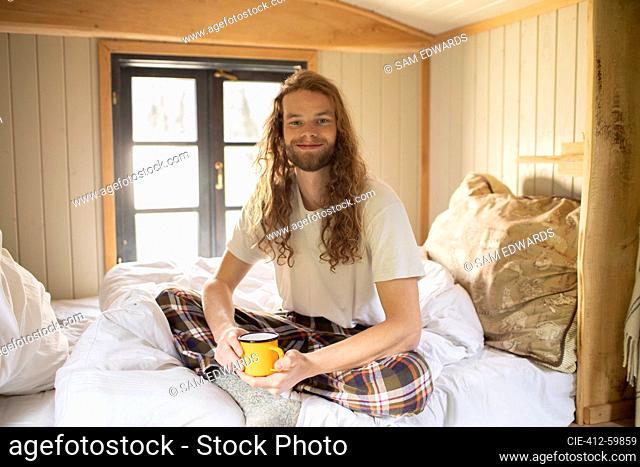 Portrait happy young man in pajamas drinking coffee in bed