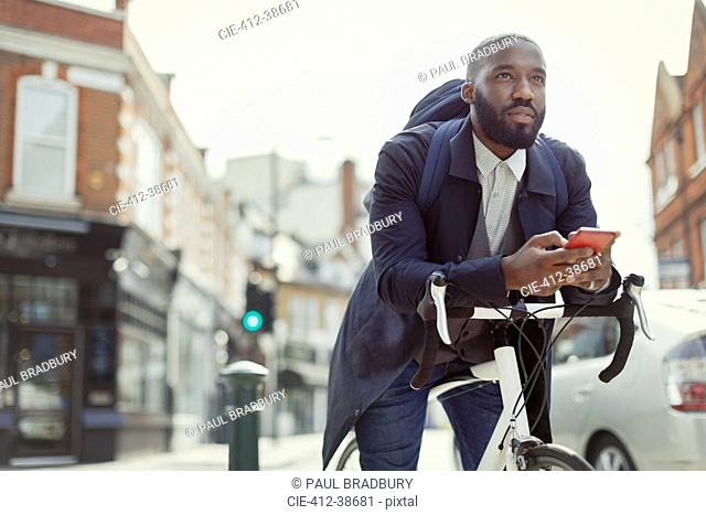 Pensive young businessman texting with cell phone, commuting with bicycle on urban street