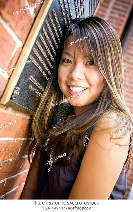 Happy young Asian female leaning on brick wall