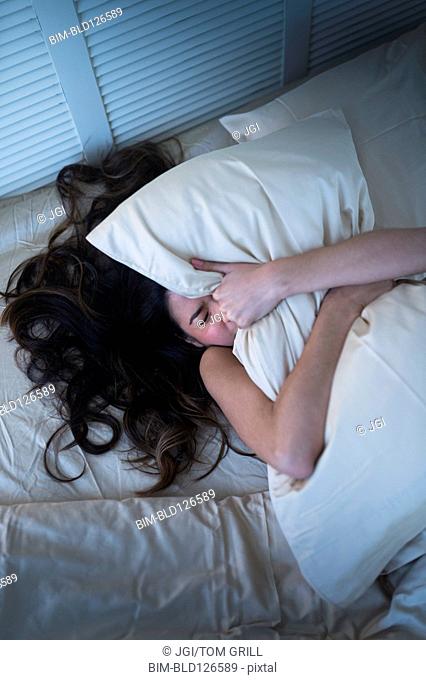 Frustrated Hispanic woman gripping pillow in bed