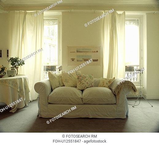 Loosecover on sofa in traditional living room with white curtains