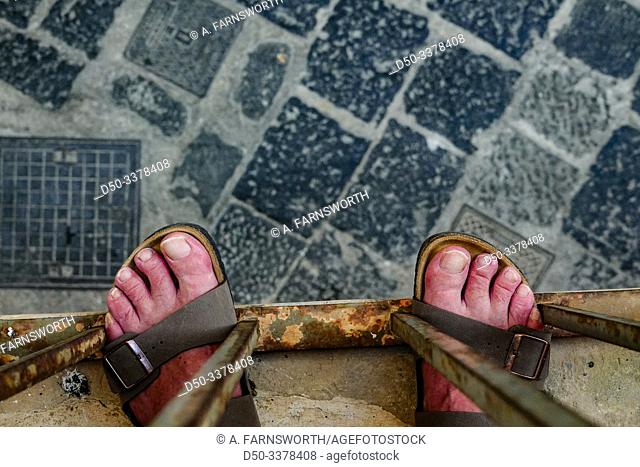 Syracuse, Sicily, Italy A man's feet with sandals on a balcony