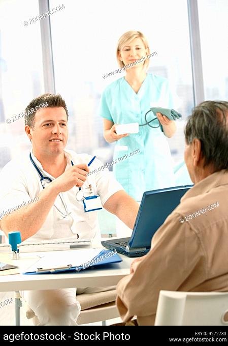 Smiling doctor discussing diagnosis with patient, smiling nurse holding blood pressure gauge