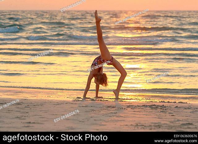 Sweet girl doing yoga on the beach over sunset sky background. Active sportive summer camp. Dancing outdoors. Healthy childhood
