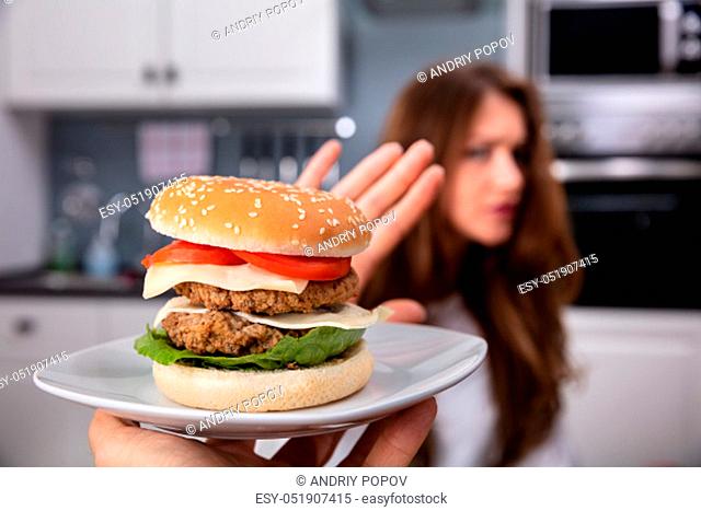 Young Woman Refusing Unhealthy Burger On Plate At Home