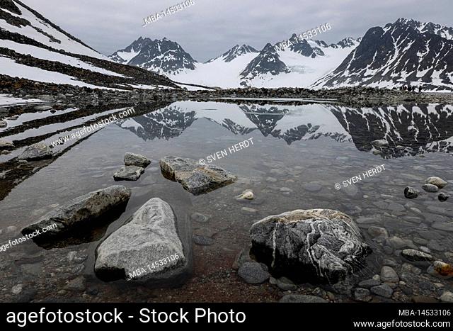 A snowy mountain range is reflected in a pool of meltwater